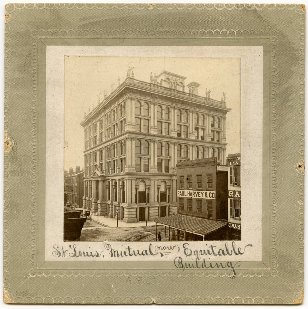 Fotografi af en seks etagers bygning med figurer langs toppen. Der er andre bygninger synlige til hver side. Bygning kaldes også St. Louis Life Insurance Building af Unknown