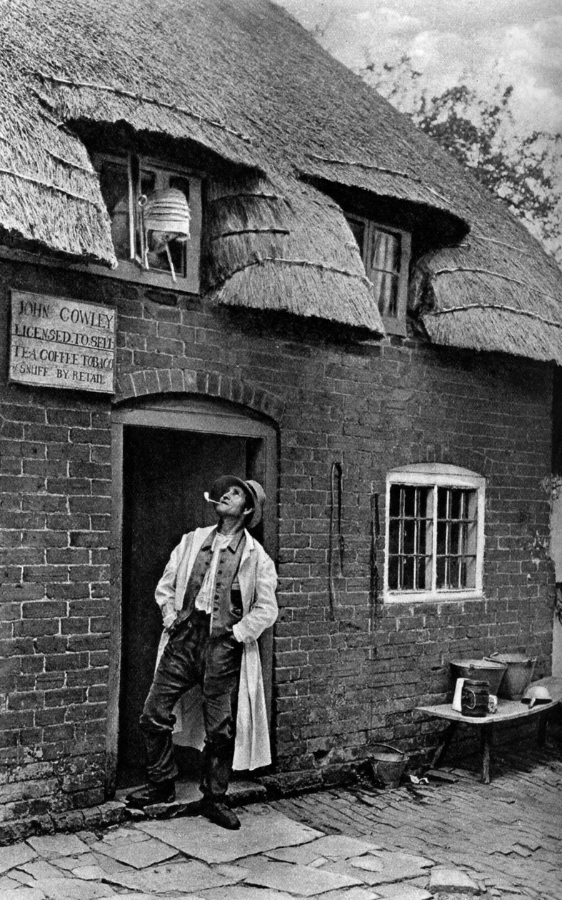 En mand, der ryger pibe uden for en butik, Worcestershire, c1922. af A. W. Cutler