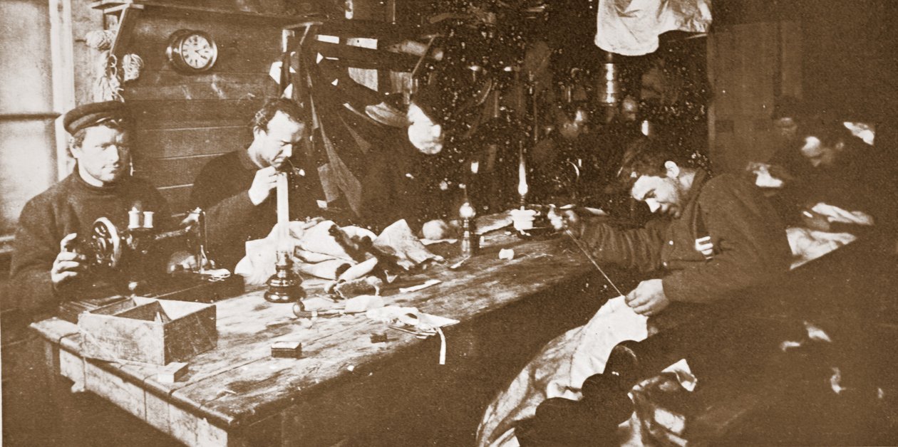 I hytten midt om vinteren beskæftigede mændene sig med at sy pels til tøj, der skulle bruges i forårets kælkning, pub. London 1907 (s/h-billede) af Anthony Fiala