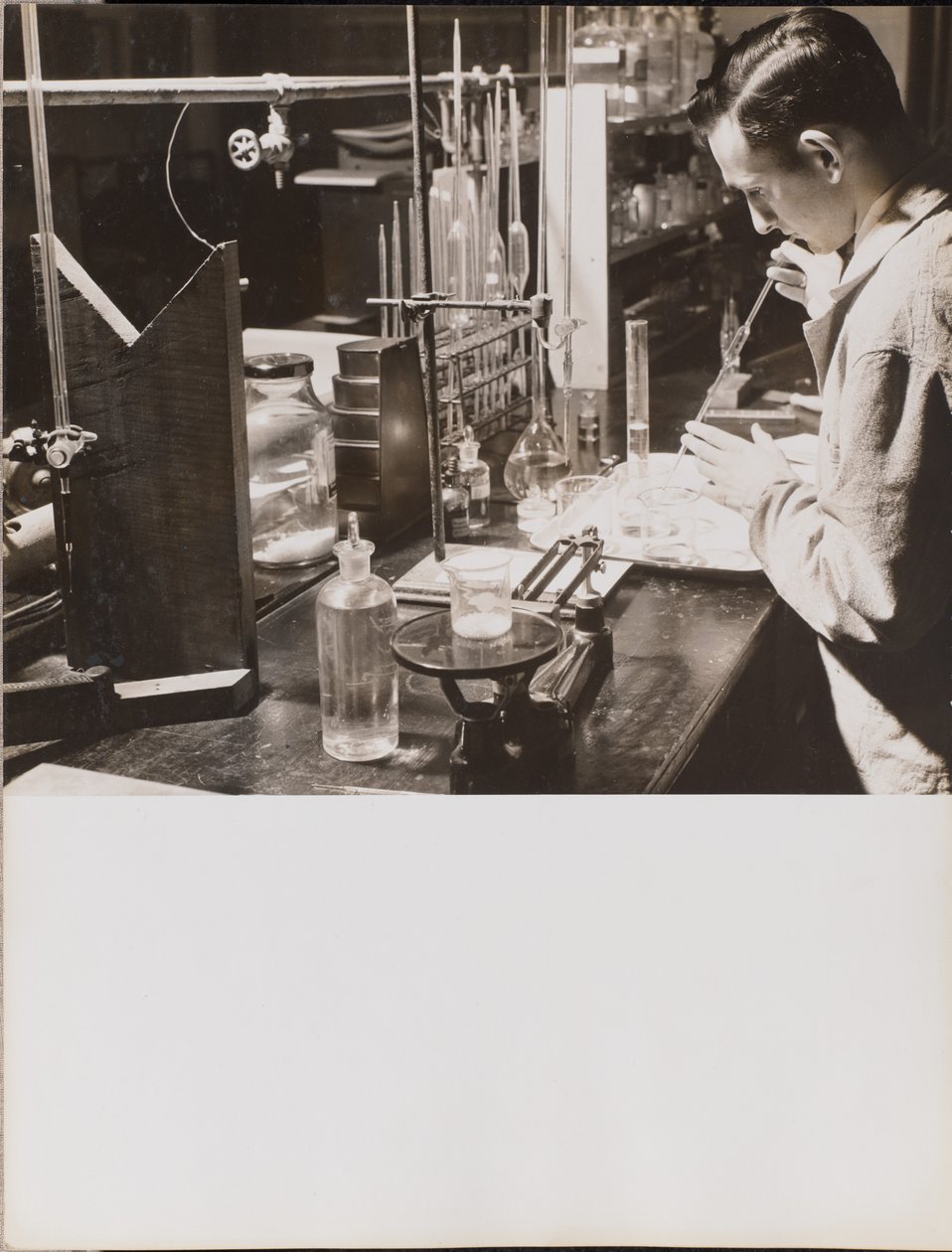 [En mand i et laboratorium bruger begge hænder til at placere en stor pipette i et bægerglas]. af Arnold Eagle