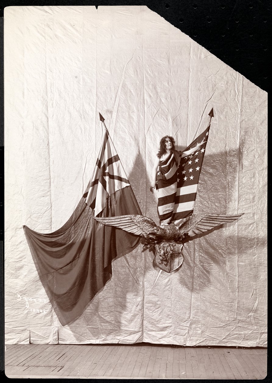 Et levende billede: en model draperet i det amerikanske flag stående oven på en skulptur af en skaldet ørn, 1900 eller 1901 (sølv gelatinetryk) af Byron Company