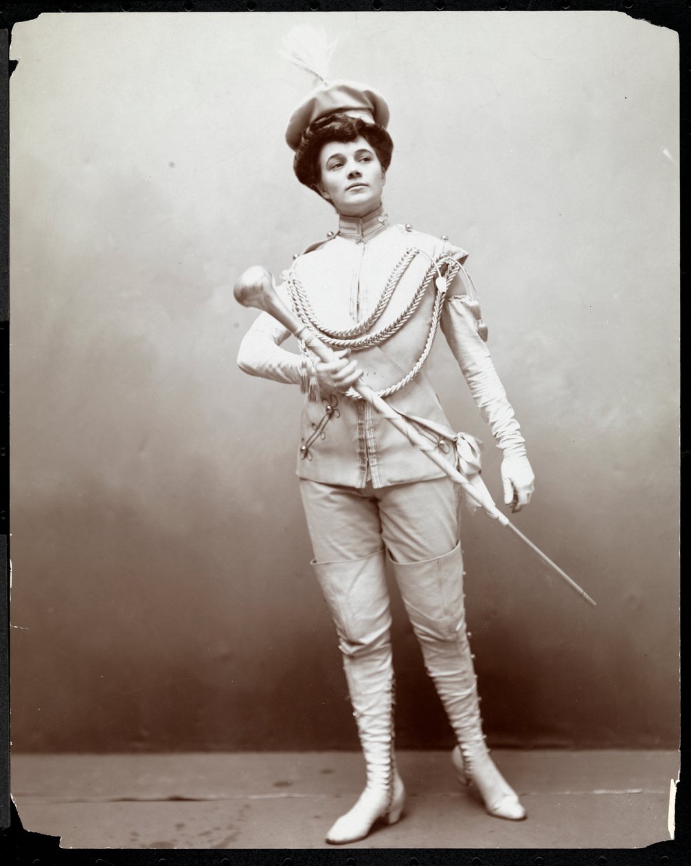 En kvinde modellerer en banduniform og holder en stafet, ca. 1898 (sølv gelatinetryk) af Byron Company