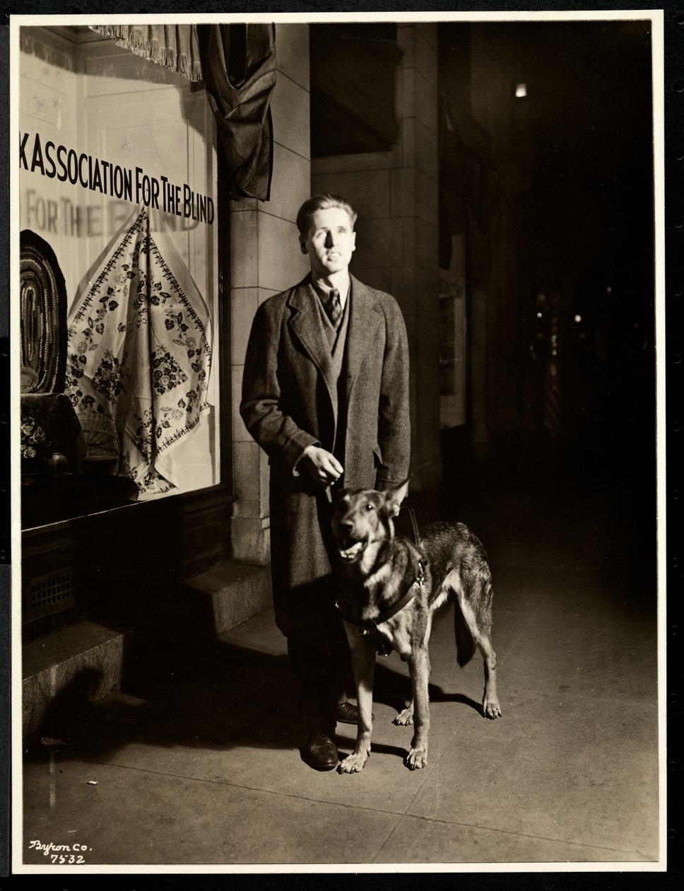 Blind mand og hans førerhund på fortovet foran New York Association for the Blind, 111 East 59th Street, New York, 1938 (sølvgelatineprint) af Byron Company