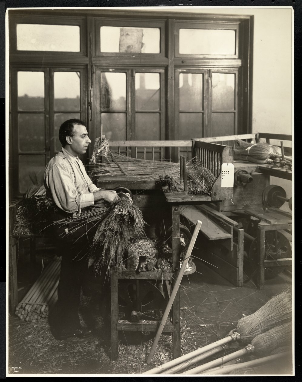Blind mand fastgør strå på kosteskafter i Bourne Memorial Building, New York, 1921 (sølv gelatinetryk) af Byron Company