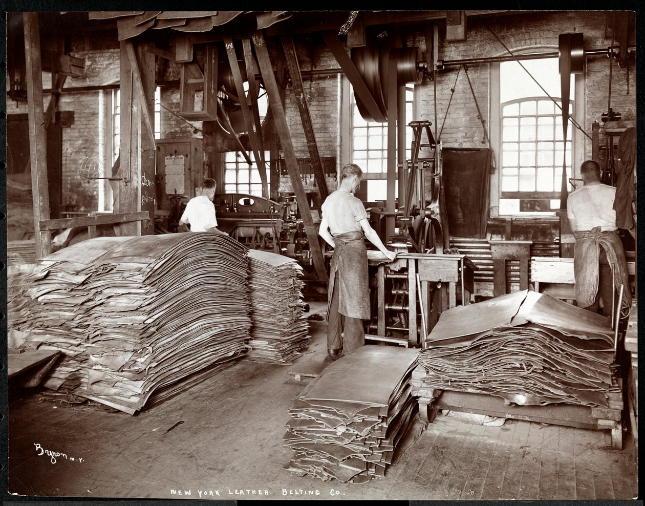 Indvendigt billede af tre mænd, der arbejder med læder og tungt udstyr på New York Leather Belting Co., New York, 1905 (sølv gelatinetryk) af Byron Company