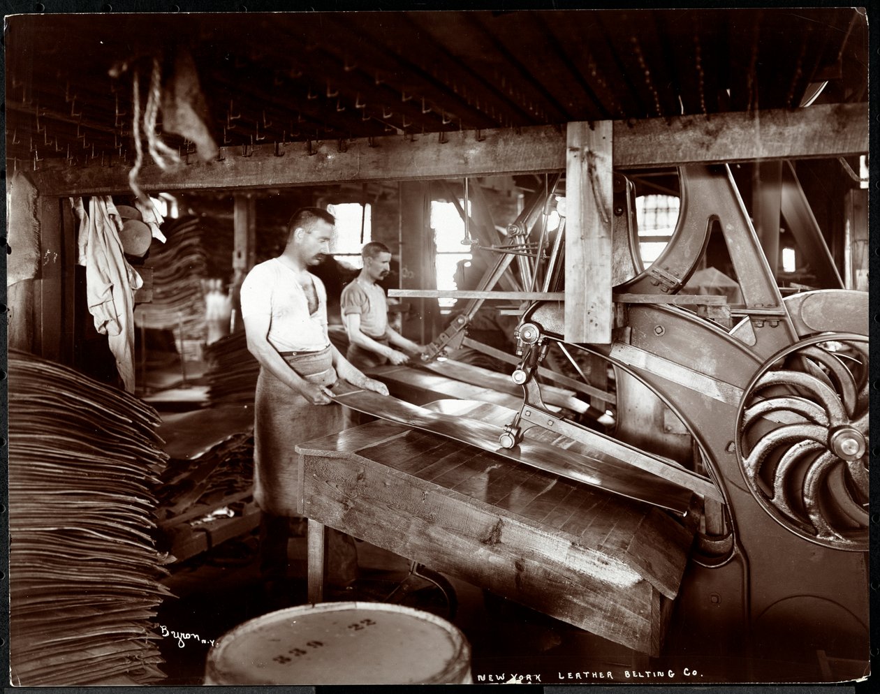 Indvendigt billede af to mænd, der arbejder med læder og tungt udstyr på New York Leather Belting Co. i New York, New York, 1905 (sølvgelatineprint) af Byron Company