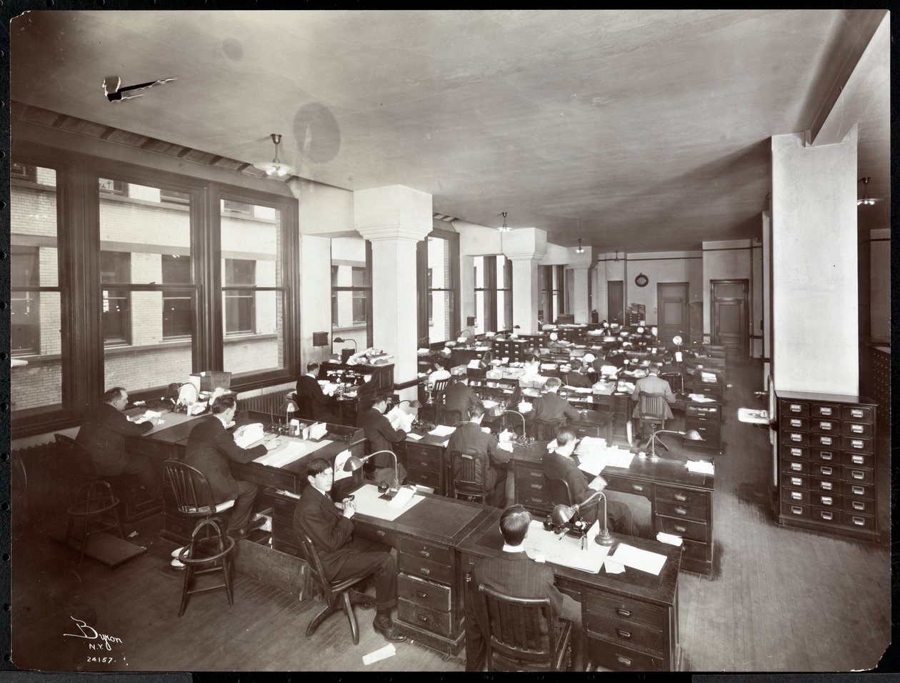 Mænd og en kvinde arbejder ved skriveborde på et kontor hos Metropolitan Life Insurance Co. på 23rd Street og Madison Avenue, New York, 1907 (sølv gelatinetryk) af Byron Company