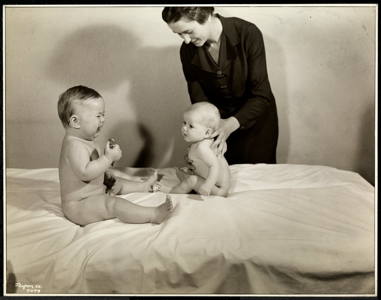 To babyer sidder op i sengen, den ene bliver støttet af en sygeplejerske, den anden holder en legetøjsbil og græder på Maternity Center Association på 70th Street East River, New York, 1935 (sølv gelatinetryk af Byron Company