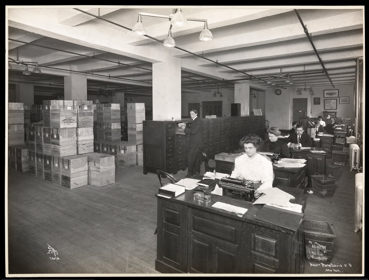 Udsigt over mænd og kvinder ved skriveborde i hvad der ser ud til at være et ekspeditionsrum hos Parke, Davis und Co., kemikere, Hudson und Vestry Streets, New York, 1910 (sølvgelatineprint) af Byron Company