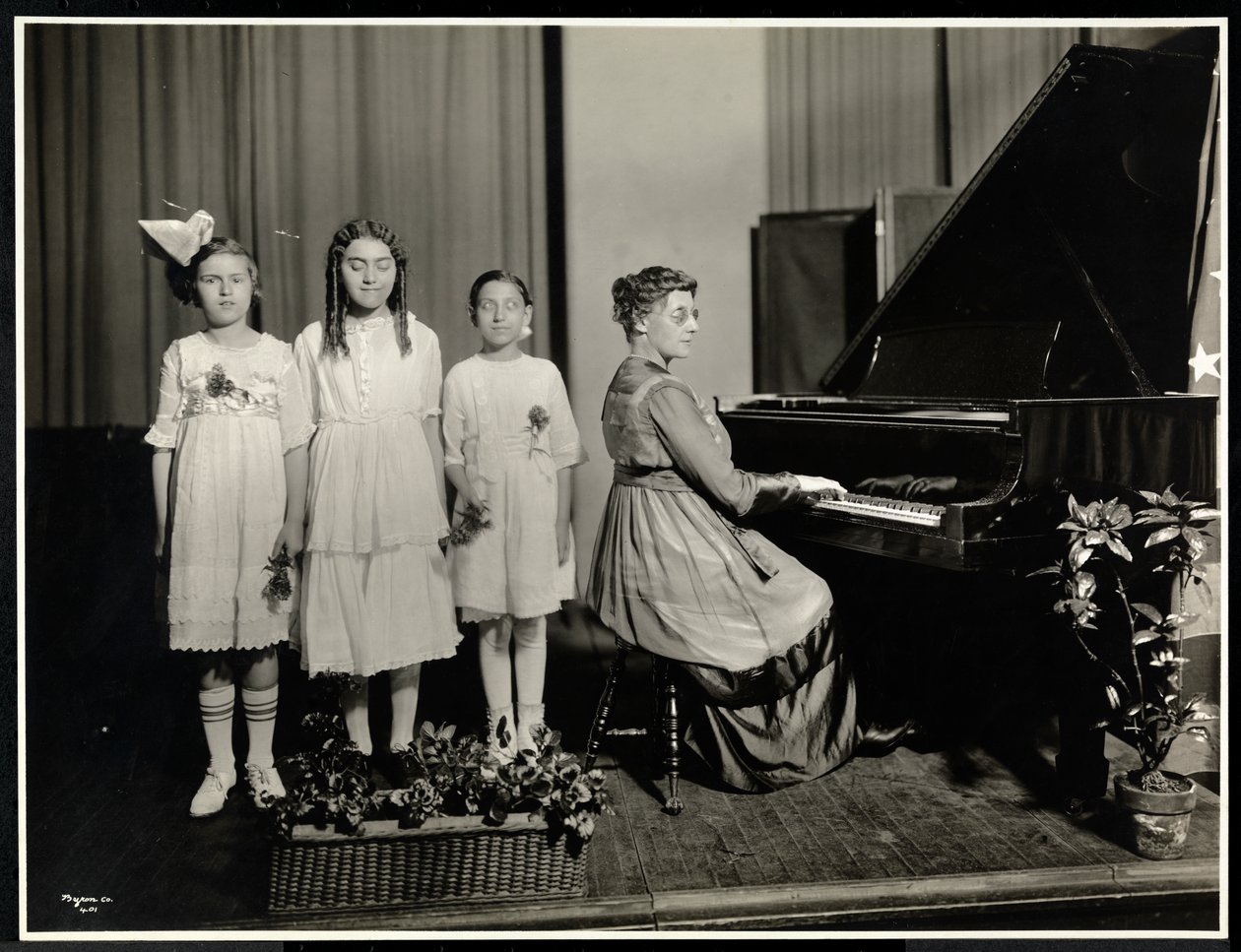 Kvinde spiller klaver, mens tre piger synger i New York Association for the Blind, 111 East 59th Street, New York, ca. 1917 (sølv gelatinetryk) af Byron Company