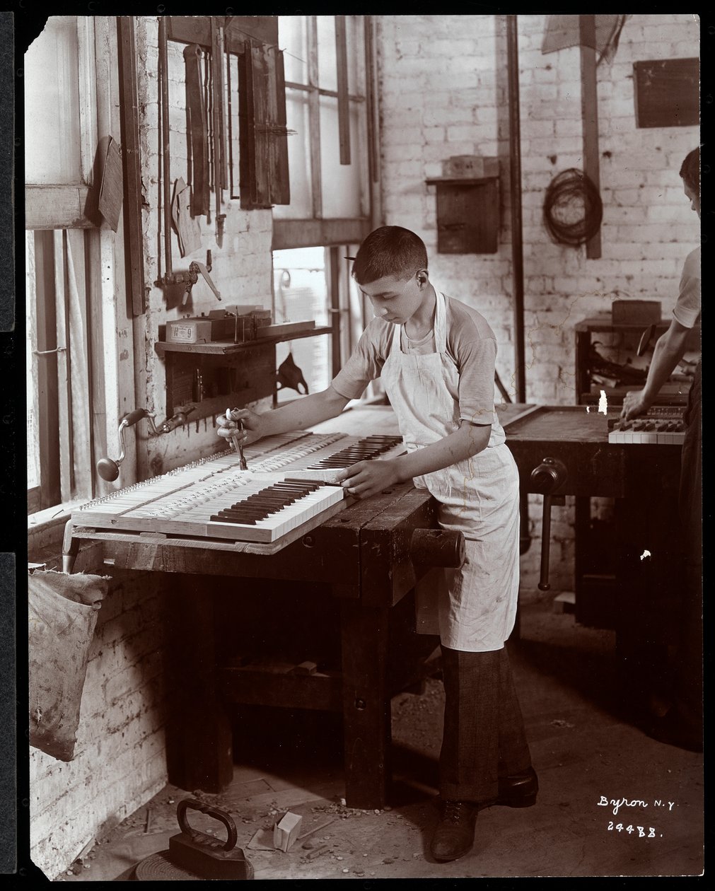 En ung mand, der arbejder på Harrington Piano Co. fabrikken, 1907 (sølv gelatinetryk) af Byron Company