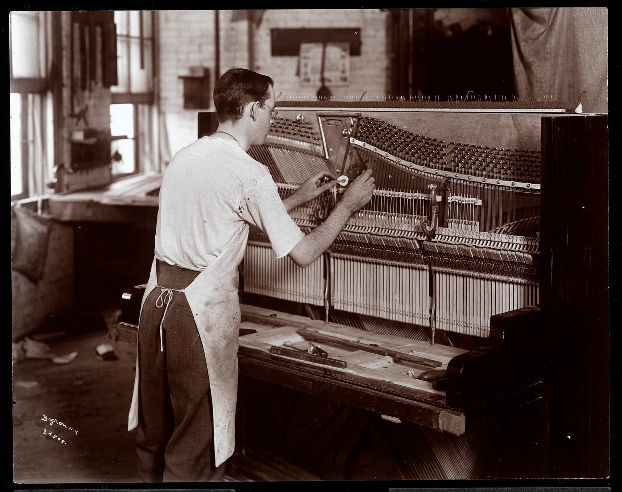 Mand, der arbejder i Hardman, Peck und Co. klaverfabrikken, New York, 1907 (sølv gelatinetryk) af Byron Company