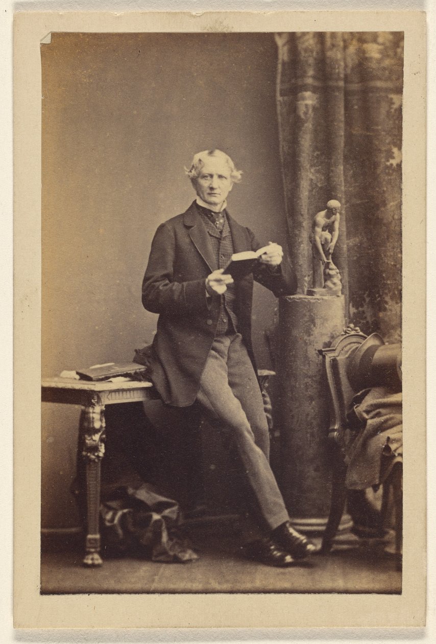 [Uidentificeret mand sidder på et bord og holder en opslået bog]. af Camille Silvy