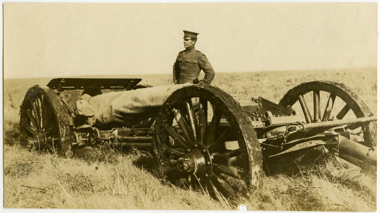 Vandret, sepia -fotografi, der viser en uniformeret mand, der står ved siden af en artilleripistol på hjul i et åbent felt af Carl Michel