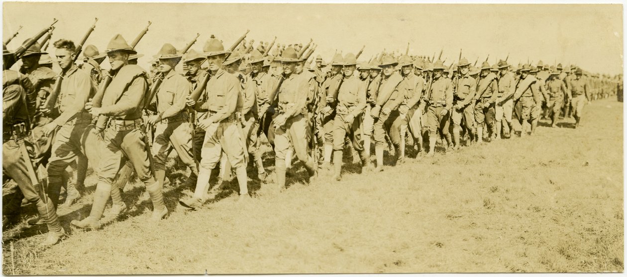 Vandret, sepia fotografi, der viser rækker af uniformerede soldater, der i formation marcherer gennem en græsmark med geværer i hånden af Carl Michel