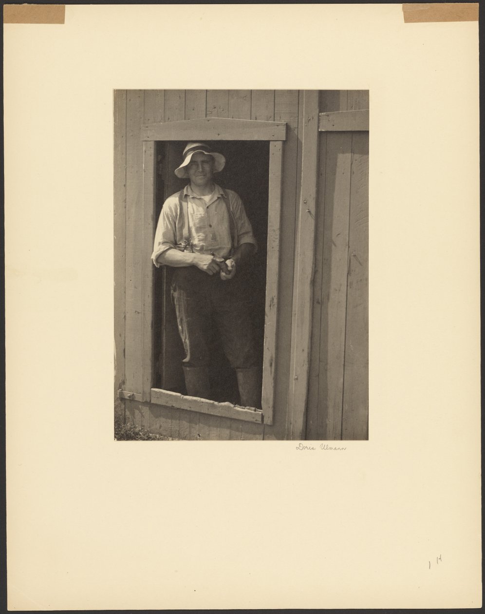 [Mand med stråhat står i døren til en lade og holder en tobakspose]. af Doris Ulmann