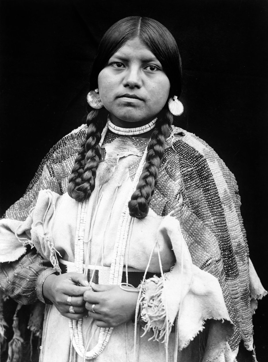 Cayuse kvinde, halvlangt portræt, stående, vendende front, fletninger, shell disk øreringe, shell perle choker og shell perler om halsen, perlebehandlet buckskin kjole med perlebælte ca. 1910, foto Edward S. Curtis af Edward Sheriff Curtis