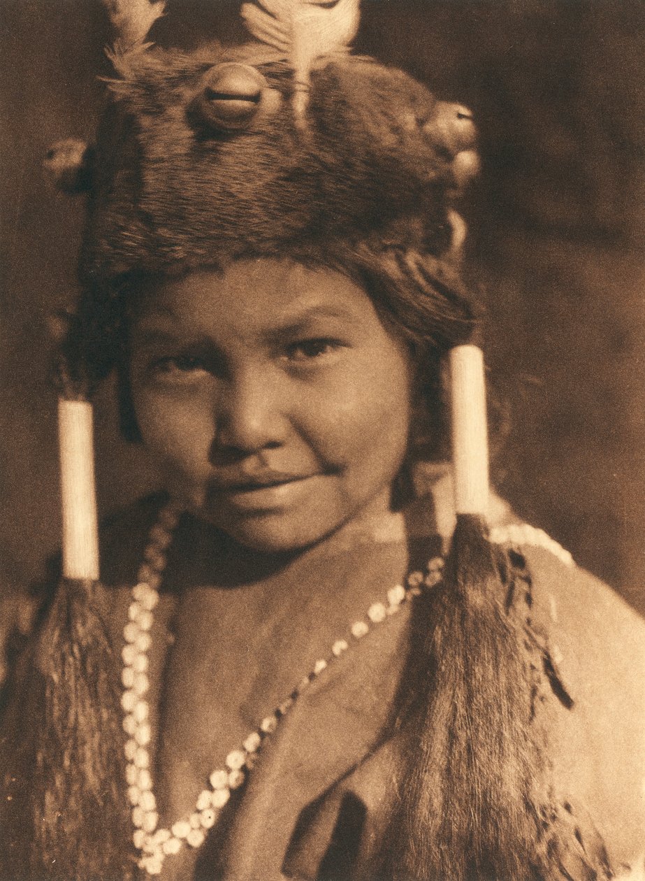 Nærbillede af en amerikansk indianerdreng fra Klamath-stammen eller -landsbyen. Han har en pelshue på med påsatte agern og fjer og bærer sit hår i to hestehaler. af Edward Sheriff Curtis