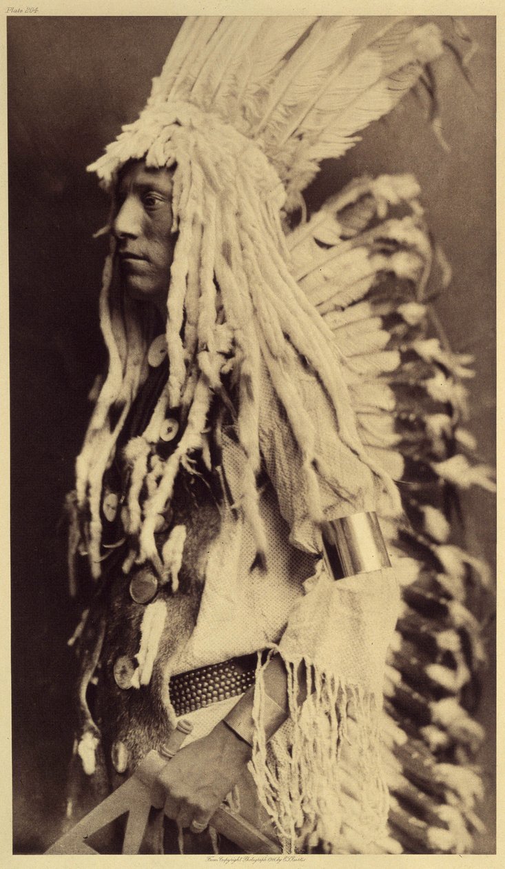 Gammel person, Piegan. Unge mænd går ikke glip af nogen anledning til offentlige festligheder for at tage deres krigerfars tøj på. Foto taget fra bind 6 af encyklopædien udgivet af Edward S. Curtis (1868-1952) om indianerne i Nordamerika, med en forgrund af Edward Sheriff Curtis