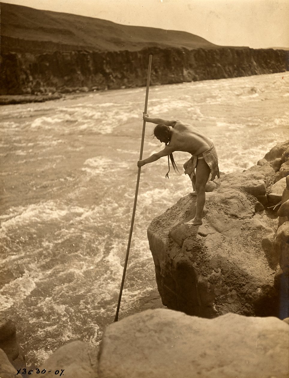 Tlakluit-indianer, stående på klippe, fisker med dykkernet, ca. 1910 (s/h-foto) af Edward Sheriff Curtis
