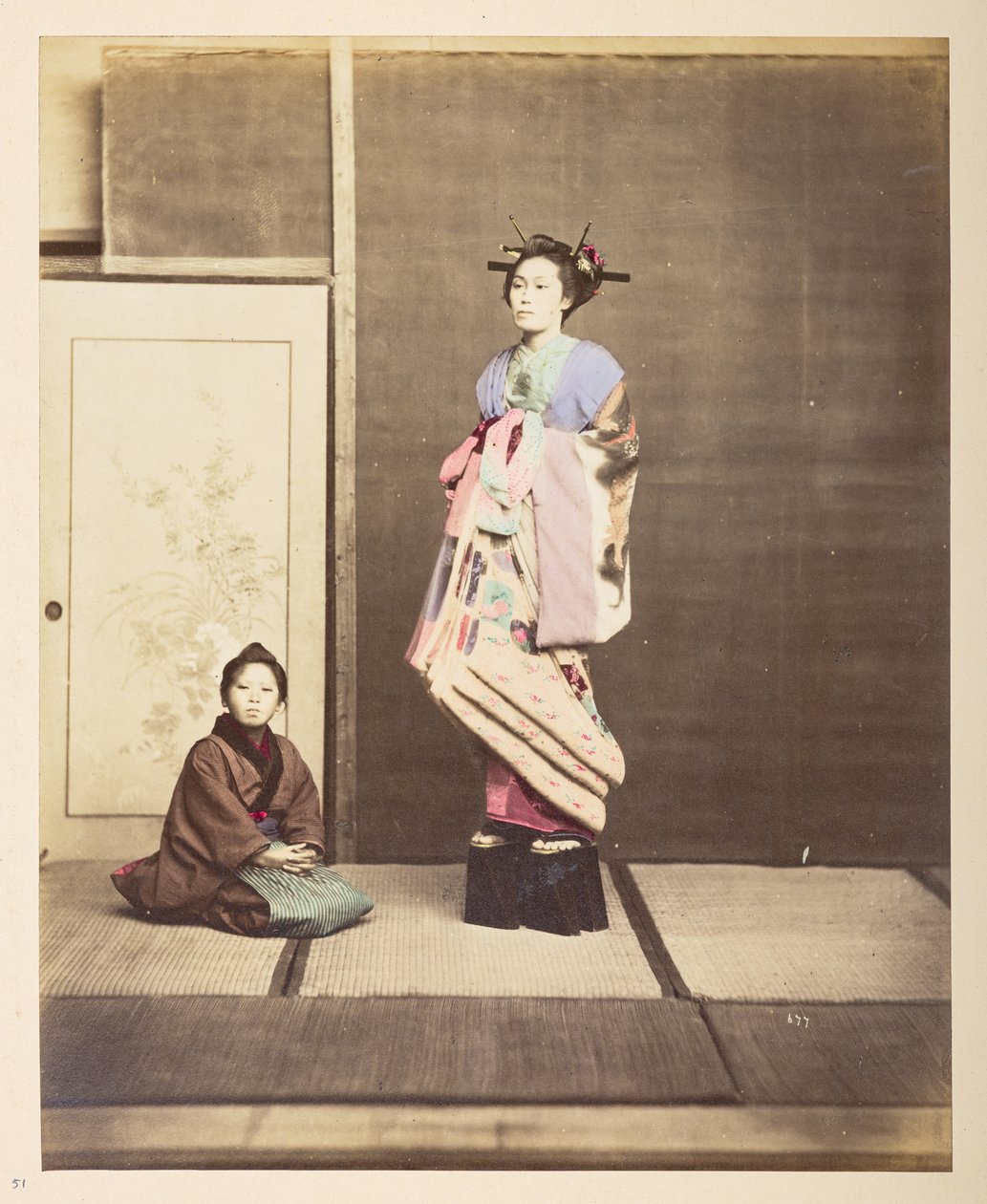 [?Geisha, ] Stående studieportræt i fuld længde af en ung kvinde i forhøjede sko, hendes unge ledsager knælende på gulvet ved siden af hende,   Fotograf: Ukendt  Lucas Collection: Fotografisk optagelse af Charles James og Morton P, Lucs verdensturné af English Photographer