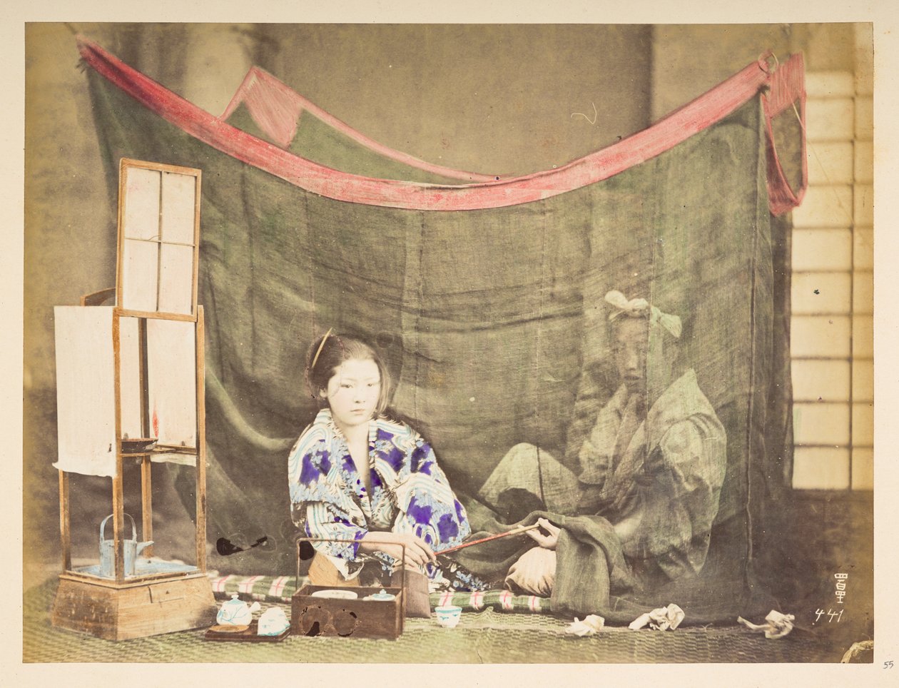 Japansk par i ro og mag, Studio-tableau af en ung japansk kvinde, siddende med telavningshinder omkring sig, og rækker en pibe til en mandsfigur, der sidder bag hende, skærmet af et linnedmyggenet,   Fotograf: Ukendt  Lucas samling: af English Photographer