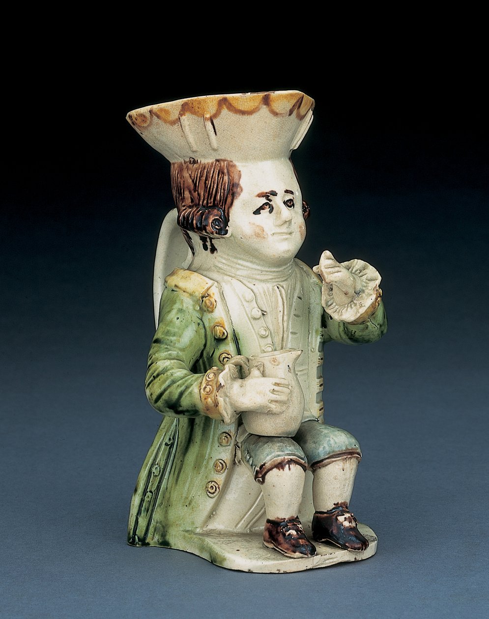 Toper toby kande, hans hat med brun og gul scalloped kant, hans indskårne brune hår i kø og med en hvid roset siddende med en baluster kande på knæet, ca. 1770 af English School