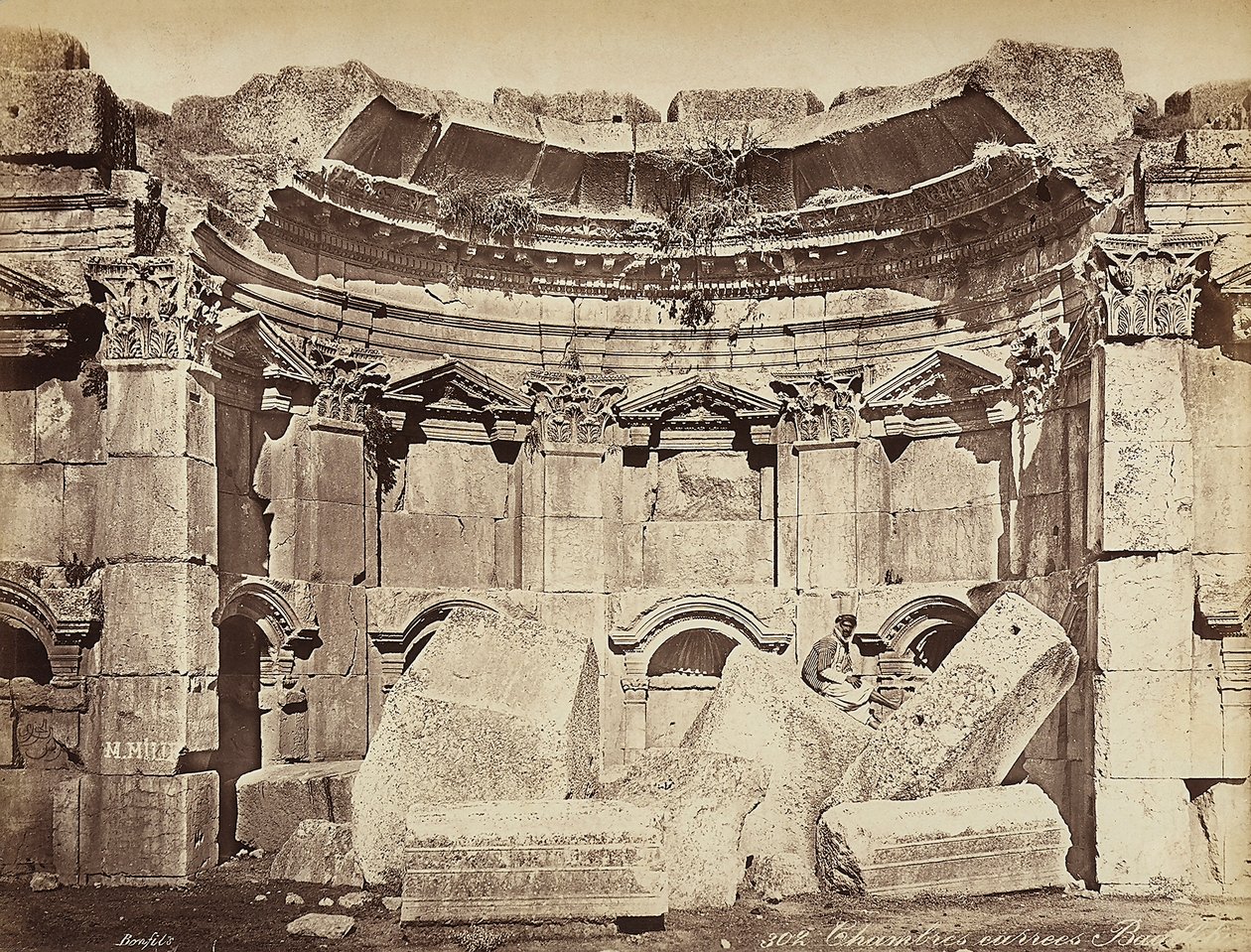 Detalje af de såkaldte "værelser" i den arkæologiske zone i Heliopolis eller Baalbek, den gamle syriske by, nu Libanon. En mand poserer, der sidder på ruinerne af Félix Bonfils