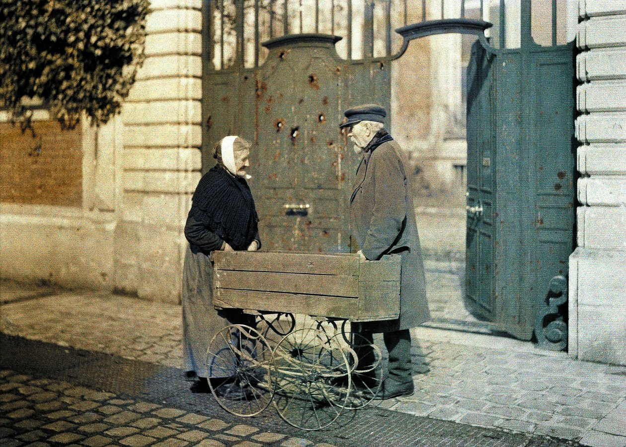 To ældre borgere fra Reims, en gammel kvinde og hr. Reiser, stående foran en port med mange skudhuller, Reims, Marne, Frankrig, 1917 (autokrom) af Fernand Cuville