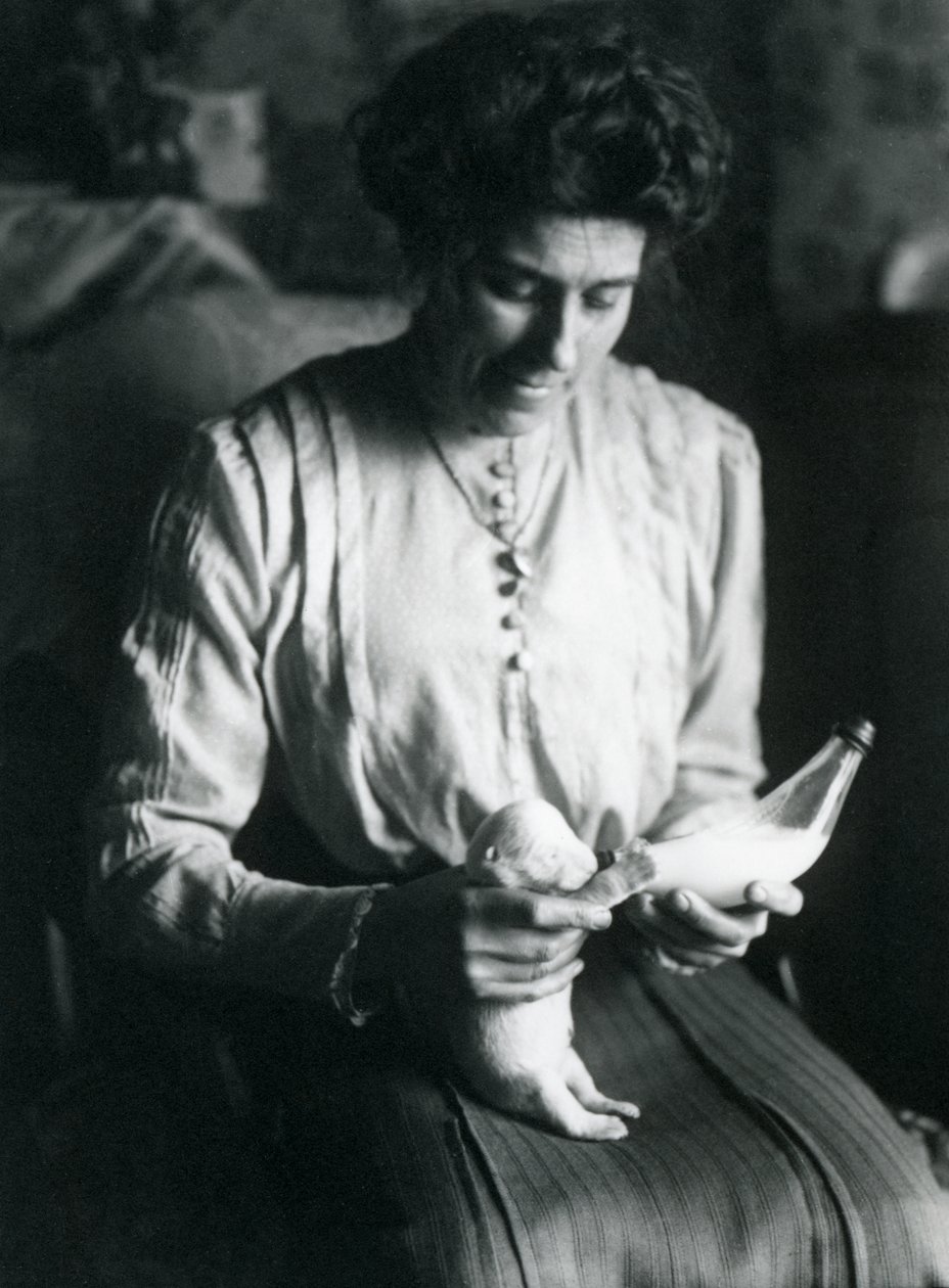 En målmands kone giver flaskemad til en nyfødt isbjørnunge, London Zoo, ca. 1914 af Frederick William Bond