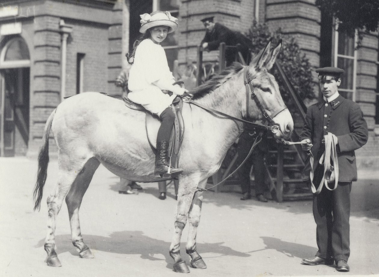 En ung dame rider på en røv, som bliver ført af en målmand, mens en anden ser på, London Zoo maj 1914 af Frederick William Bond