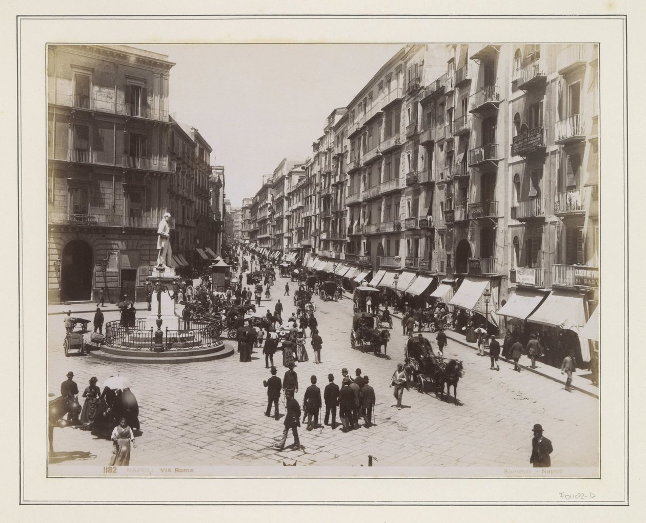 Udsigt over Via Roma i Napoli med en statue, butikker, hestevogne og forbipasserende af Giorgio Sommer