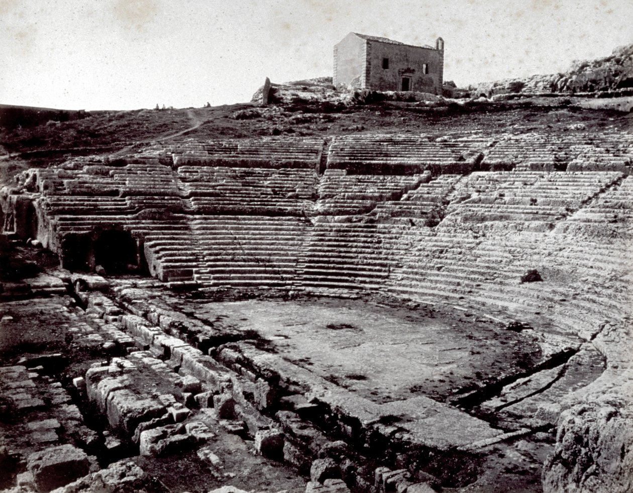 Resterne af det græske teater i Siracusa i Neàpolls monumentale park. I forgrunden det halvcirkelformede orkester og caveaen af Giorgio Sommer