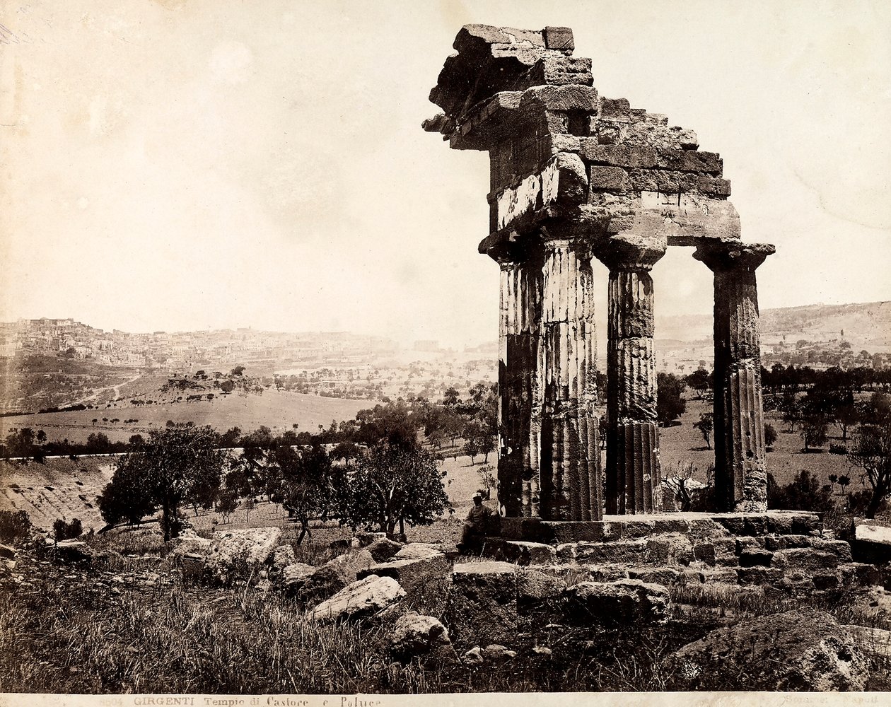 Udsigt over de resterende fire søjler, der understøtter en entablatur af Castor- og Pollux-templet i Valle dei Templi, Agrigento. Et panorama af byen er synligt i baggrunden af Giorgio Sommer