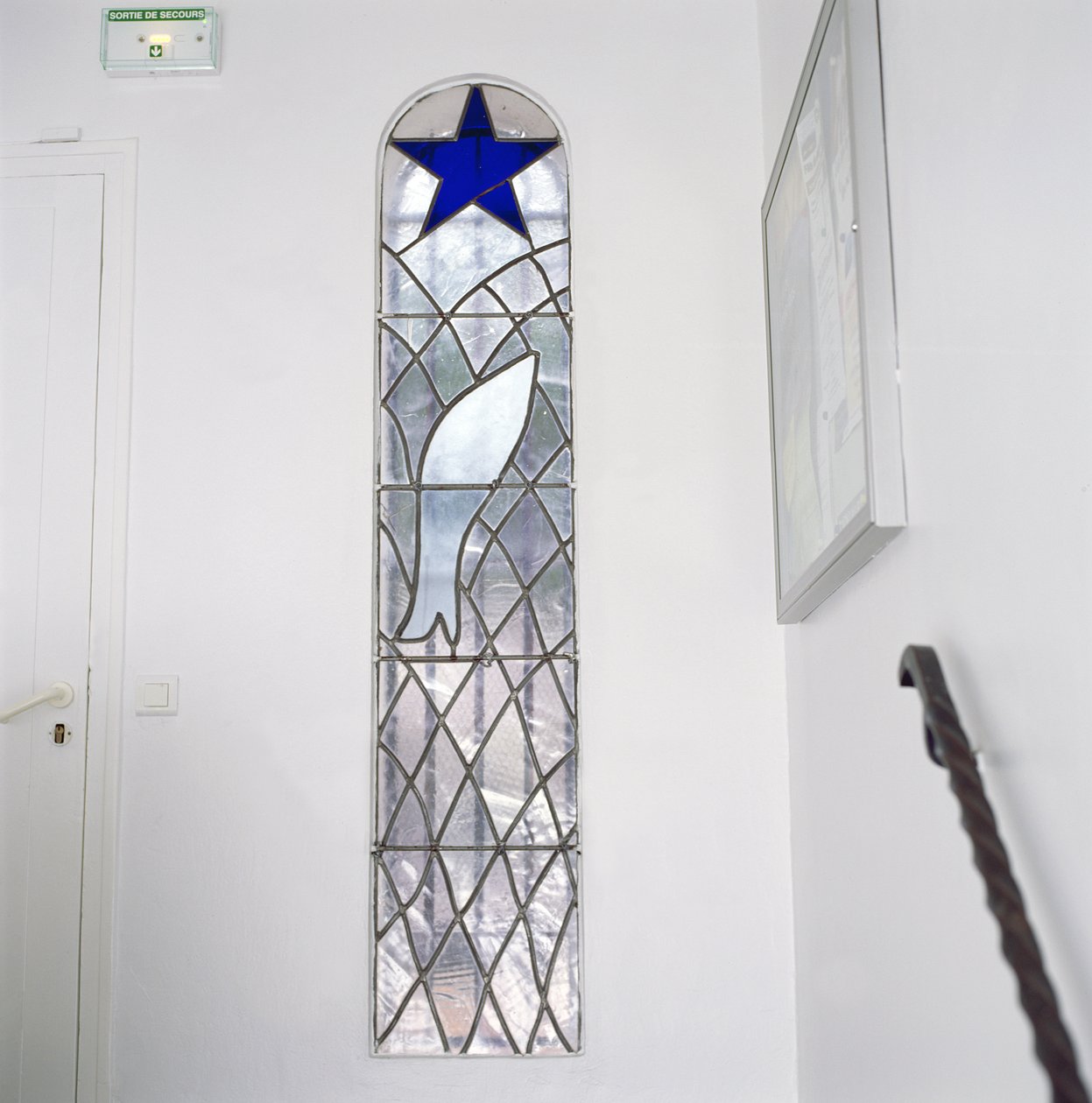 Glasmosaikvindue med en fisk fanget i et net under Frelsens Stjerne, fra trappen, der fører til Rosenkransens Kapel. af Henri Matisse