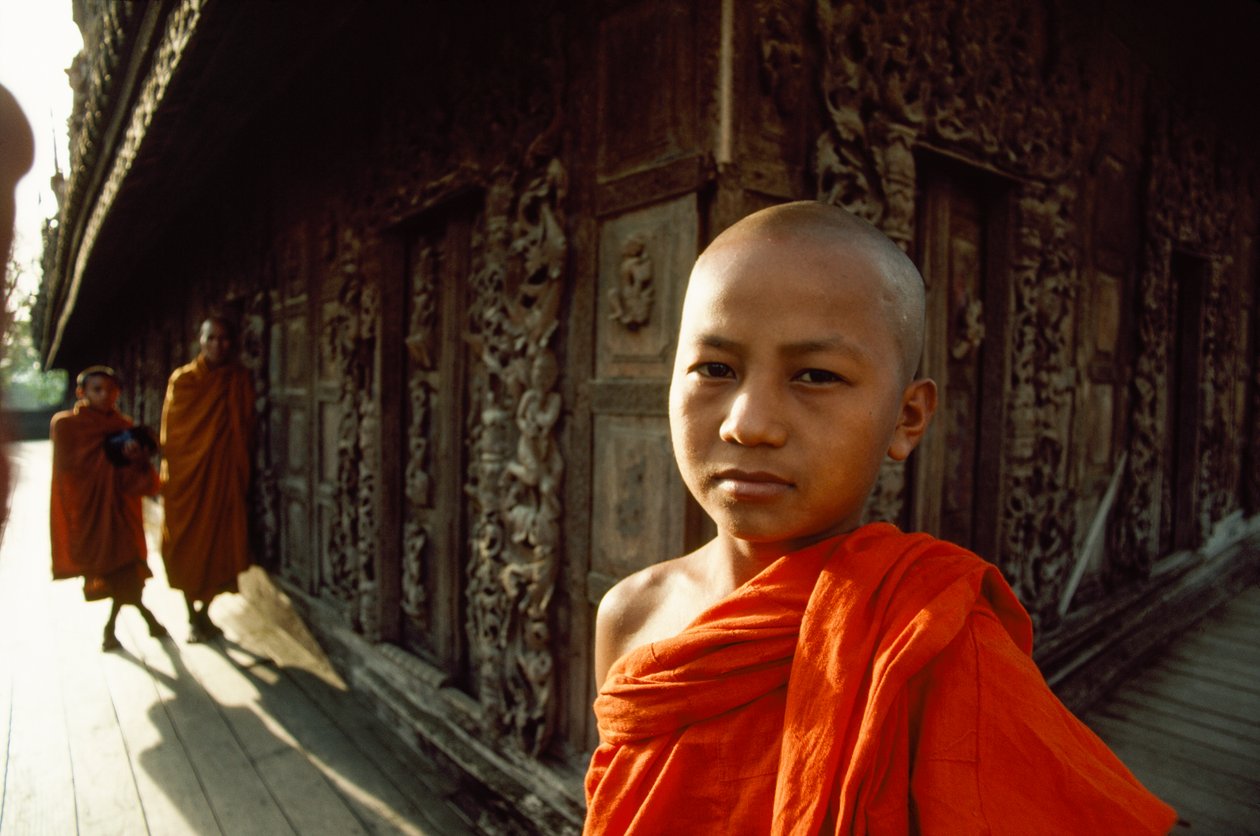 En ung novicemunk foran udskårne teaktræspaneler. Shwenandaw-klosteret, Mandalay, Burma. af James L Stanfield