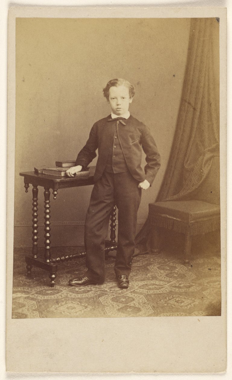 [Uidentificeret lille dreng i jakkesæt står ved et bord med bøger ovenpå]. af Joseph Brown