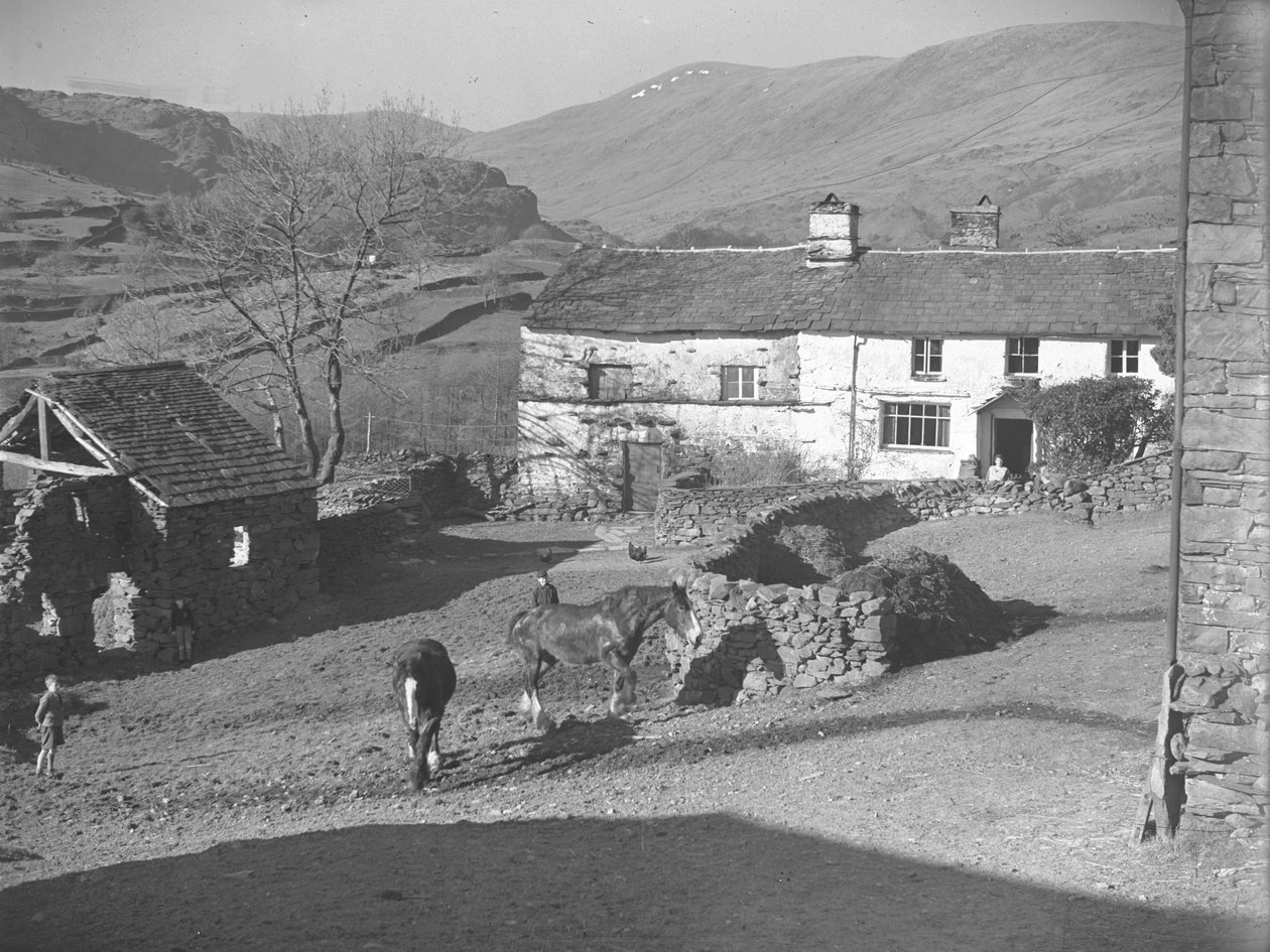 Tre unge drenge ser på heste på gårdspladsen i Kentmere med stuehus og fjelde bagved af Joseph Hardman