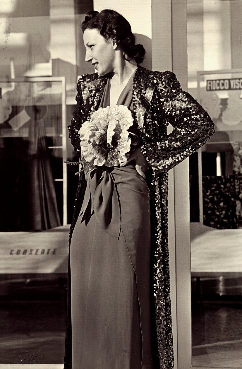 Model i aftenkjole skabt af det italienske couture-hus "Dragoni". Artiklen er pyntet med en imponerende blomst og suppleret med en overfrakke med pailletter. (s/h foto) af Luis Bogino