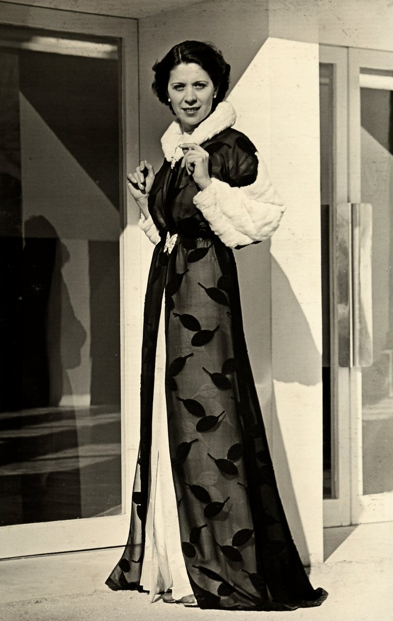 Model bærer aftenkjole skabt af det italienske couture-hus "Bernasconi". Den præsenterede artikel består af en chiffonoverfrakke med pelskantet krave og manchetter (s/h foto) af Luis Bogino