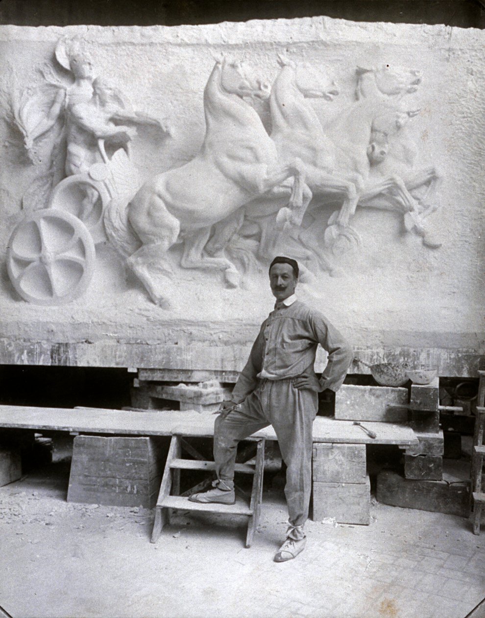 Portræt i fuld længde af den berømte billedhugger Pietro Canonica. Han poserer i sit studie foran et marmorhøjrelief, han arbejder på (s/h-foto) af Mario Nunes Vais