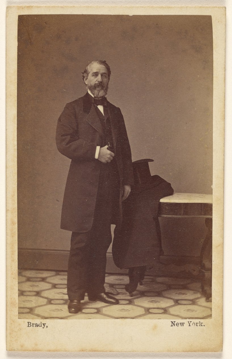 [En ukendt, skægget mand står op; en høj hat og en frakke ligger på et bord i nærheden] af Mathew B. Brady