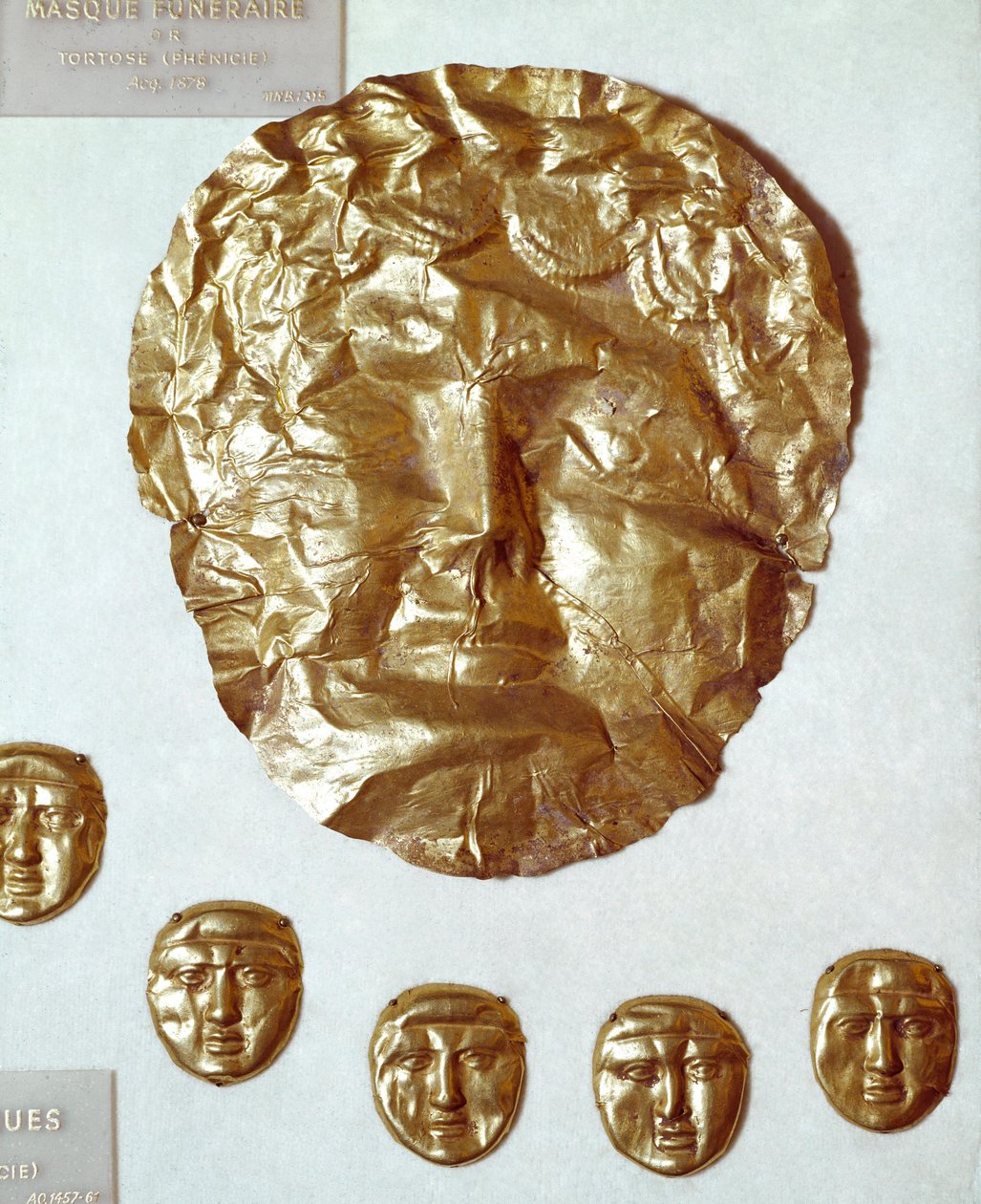 Fønikisk kunst: stor maske af bladguld på kvindens ansigt og gruppe af fem små guldmasker nedenfor af Phoenician Phoenician