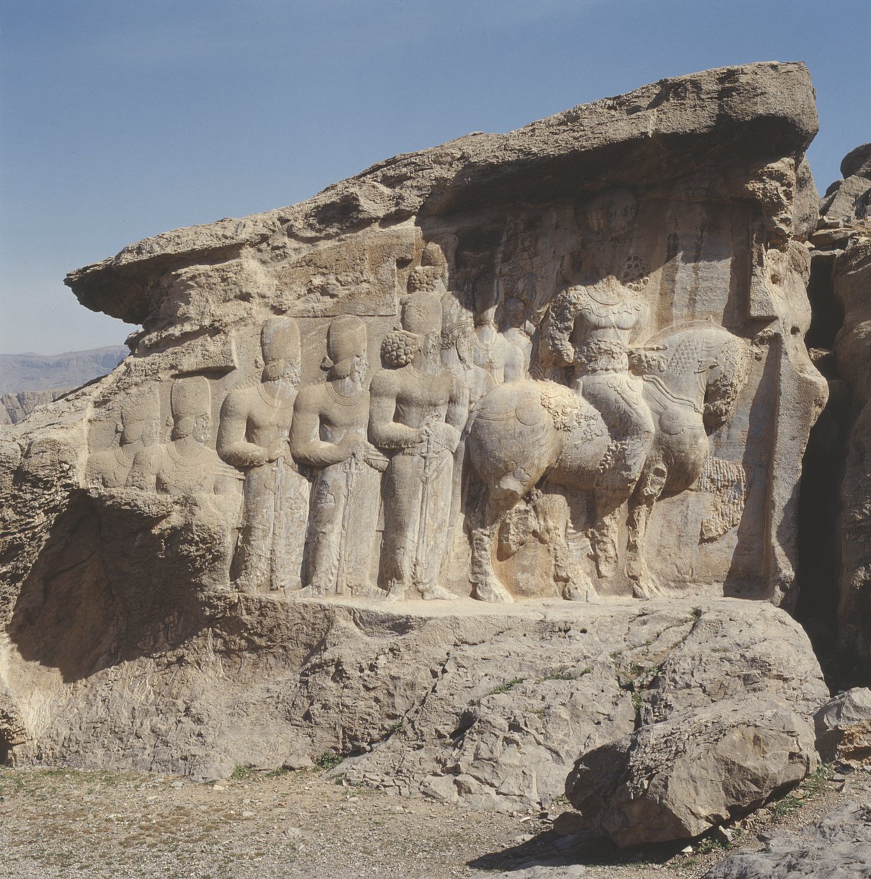 Klipperelief, der forestiller Shapur I (241-72 e.Kr.) og hans familie med heraldiske emblemer på deres hatte med en tresproget inskription på hesten på græsk, parthisk og mellempersisk af Sasanian