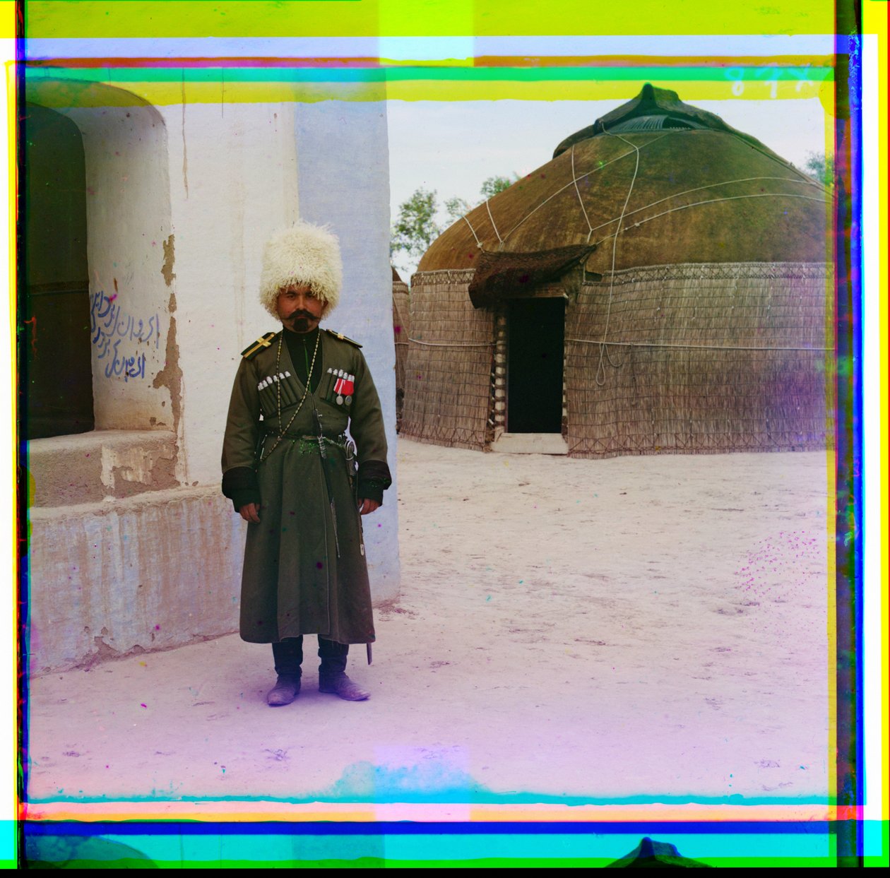 En bevæbnet mand i uniform står ved siden af bygningen med en jurte i baggrunden, Rusland, 1915 af Sergey Prokudin Gorsky