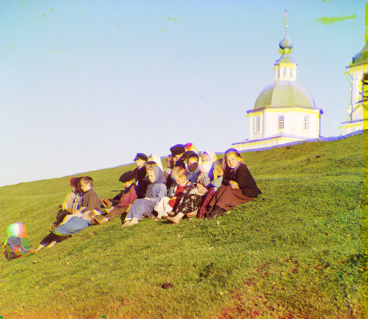 Russiske børn sidder på siden af en bakke nær en kirke og klokketårn på landet nær White Lake, i det nordlige europæiske Rusland, 1905-1915 af Sergey Prokudin Gorsky