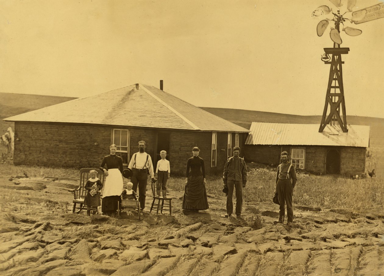 Familie af husmænd uden for deres torvhus med en vindmølle på taget af den tilstødende bygning i Custer County, Nebraska, ca. 1885 (s/h-foto) af Solomon D. Butcher