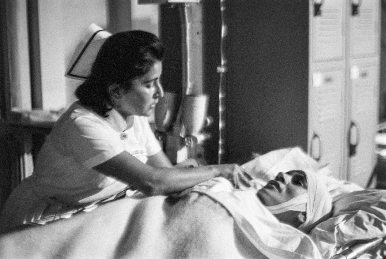 En sygeplejerske hjælper en patient, der ligger udstrakt efter en operation på hospitalsskibet SS Hope. af Ted Spiegel