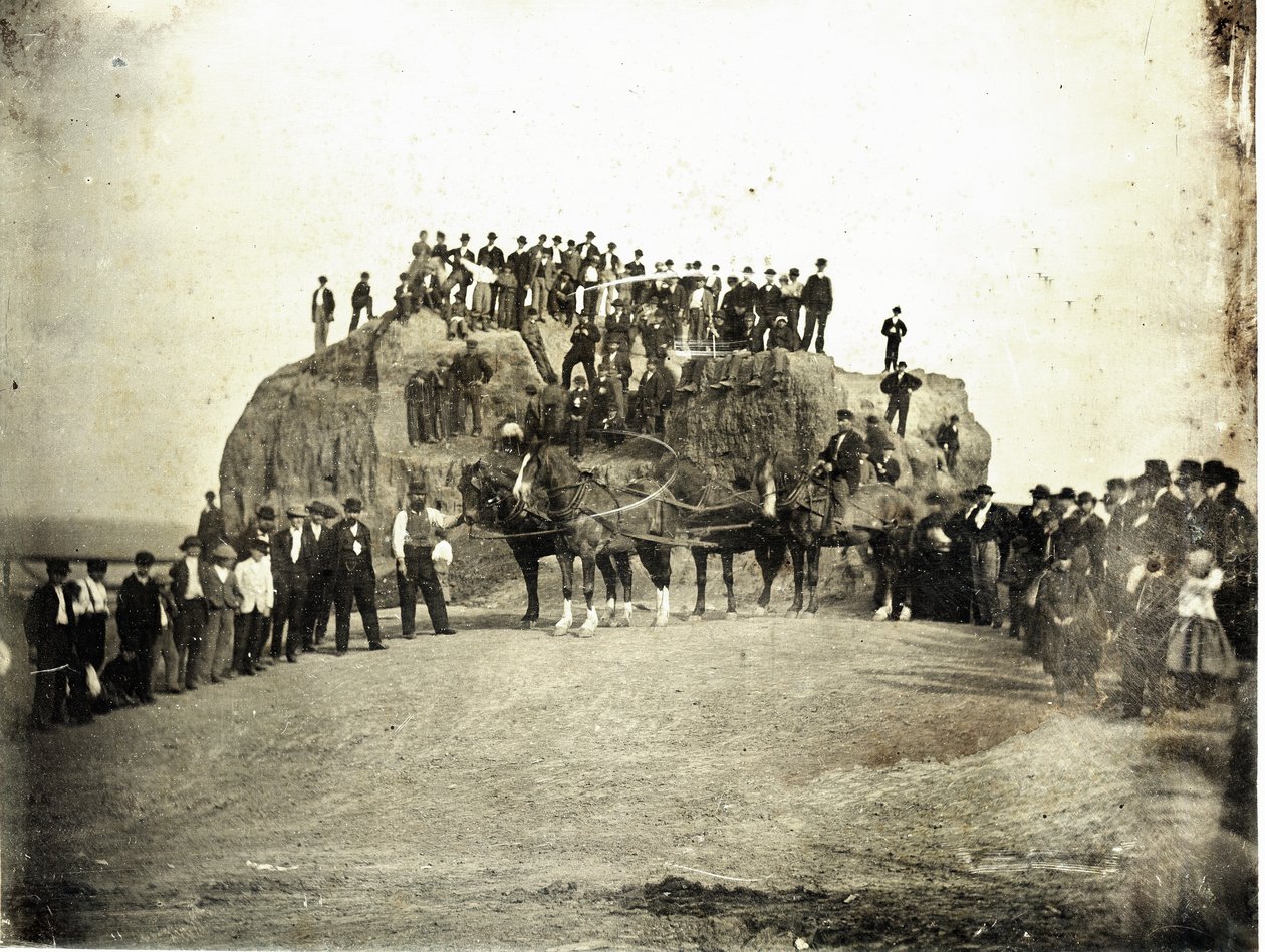 En flok mænd, børn og nogle få heste står på toppen af og foran Big Mound, som er vist delvist gruset. af Thomas M. Easterly