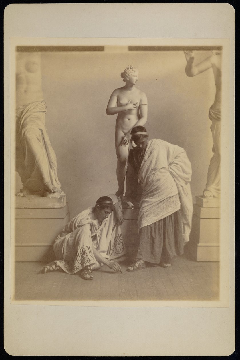[To mandlige studerende i græsk kostume foran en gipsafstøbning af Afrodite i afstøbningsrummet på Pennsylvania Academy]. af Thomas Eakins